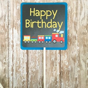 May include: A blue chalkboard sign with the text "Happy Birthday" in yellow letters. A train with colorful cars and a red engine is pictured below the text.