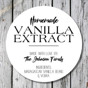 Op de afbeelding: Een wit, rond etiket met de zwarte woorden "Homemade VANILLA EXTRACT". De tekst "MADE WITH LOVE BY: The Johnson Family" is opgenomen, evenals de ingredi&euml;nten: Madagascar vanillebonen en wodka.
