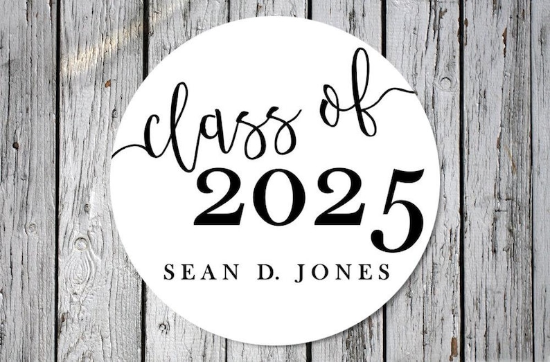 May include: A white circular sticker with black text. The words "class of" are in a cursive font above the bold numbers "2025". Below the numbers is the name "SEAN D. JONES" in a simple, sans-serif font. The background is a weathered wood.
