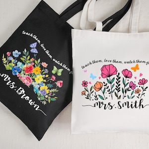 Puede incluir: Dos bolsas de mano, una negra y otra blanca, con diseños florales y el texto "teach them, love them, watch them grow". La bolsa negra dice "Mrs. Brown", y la blanca dice "Mrs. Smith".