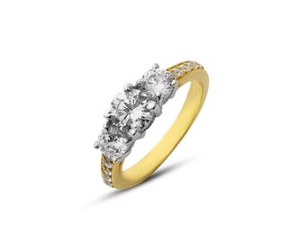 May include: A gold and silver ring featuring three clear, round gemstones. The gold band has small clear stones set along the top. The ring is set against a white background.
