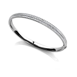 Pode incluir: Uma pulseira de prata com duas fileiras de pequenas pedras preciosas brilhantes. A pulseira tem um design curvo e uma superfície polida e reflexiva, criando uma aparência brilhante e elegante. As pedras preciosas são uniformemente espaçadas.
