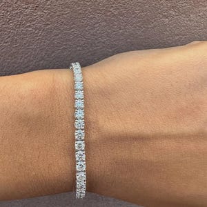 Peut inclure: Un bracelet de tennis orné d'une ligne de diamants ronds étincelants. Le bracelet est serti dans un bracelet en argent ou en or blanc et est porté au poignet. Les diamants sont clairs et réfléchissent la lumière.
