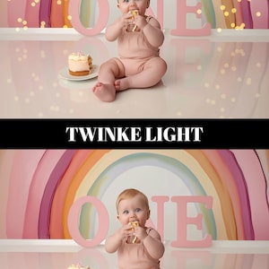 May include: A baby in a pink romper sits in front of a rainbow backdrop, eating a piece of cake. The word "ONE" is spelled out in large pink letters. A small cake sits on a white plate. Twinkle lights are in the background.