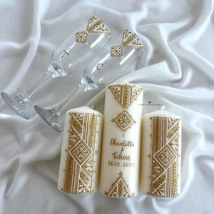 Peut inclure: Ensemble de mariage élégant comprenant deux flûtes à champagne et trois bougies piliers. Les flûtes ont des motifs géométriques dorés et les lettres "T" et "C". Les bougies sont blanches avec des motifs géométriques dorés et les noms "Charlotte & Tahan" et la date "26.12.2025".