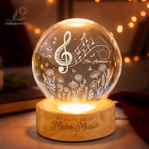Pu&ograve; includere: Una sfera di vetro luminosa con note musicali e motivi floreali, appoggiata su una base di legno. La base recita "IT'S A GOOD DAY TO Make Music". La sfera &egrave; personalizzata con il nome "Mrs. Anderson".