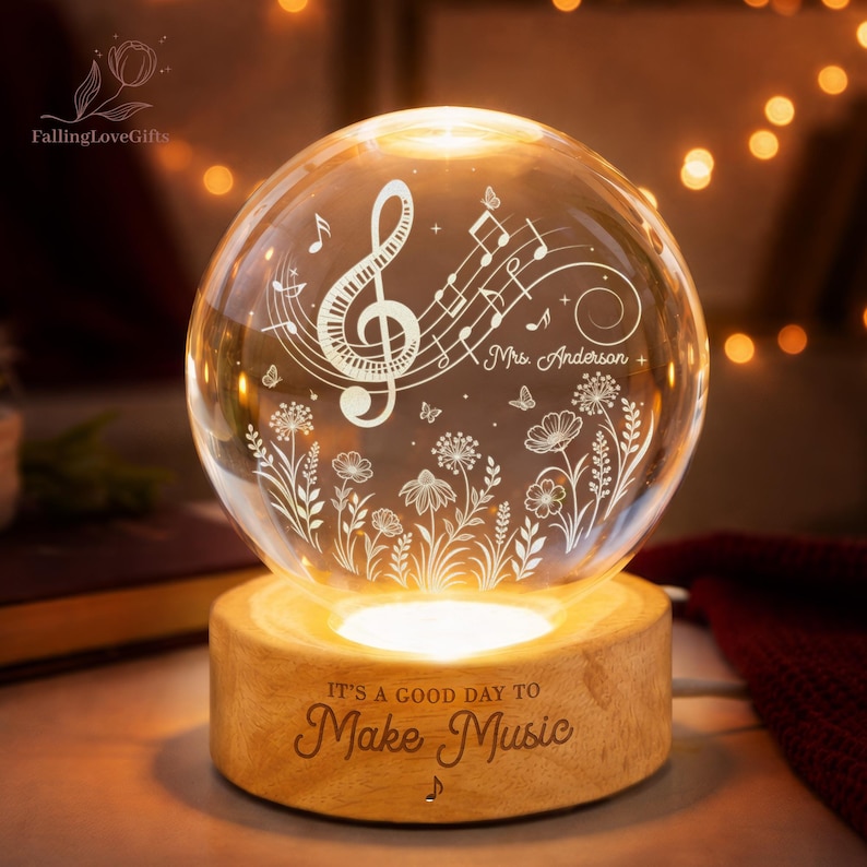 Pu&ograve; includere: Una sfera di vetro luminosa con note musicali e motivi floreali, appoggiata su una base di legno. La base recita "IT'S A GOOD DAY TO Make Music". La sfera &egrave; personalizzata con il nome "Mrs. Anderson".