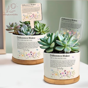 May include: Two white ceramic succulent planters with bamboo saucers. Each planter has a floral design and the words "Difference Maker" and "Wesley" printed on it. A wooden sign with the same text is placed in the soil.