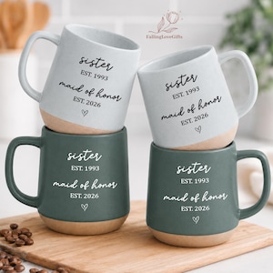 May include: Four ceramic mugs with handles, two in light gray and two in dark green, featuring a tan base. Each mug is printed with the text "sister EST. 1993 maid of honor EST. 2026" and a small heart icon. The brand logo "FallingLoveGifts" is visible.