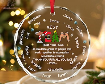 May include: A circular clear glass Christmas ornament with a red ribbon hanger. The center features the text BEST TEAM with a Santa hat, Christmas tree, and gingerbread man graphic, followed by a definition and the year 2026, surrounded by names.