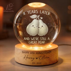 May include: A spherical glass night light on a round wooden base. The glass features two illustrated pears with faces, the text 4 YEARS LATER AND WE'RE STILL A GREAT PEAR, and the base reads HAPPY 4TH ANNIVERSARY, Harry, Olivia, and EST. 2022.