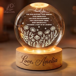 May include: A clear glass sphere lamp resting on a cylindrical wooden base. The sphere features etched floral designs, butterflies, and the text: Thank You... FOR YOUR SUPPORT, YOUR WISDOM, YOUR INSPIRATION, AND YOUR ENCOURAGEMENT. FOR ALWAYS BEING THERE. MOST IMPORTANTLY, FOR BEING A PART OF MY JOURNEY. The wooden base is engraved with the text: Love, Amelia.