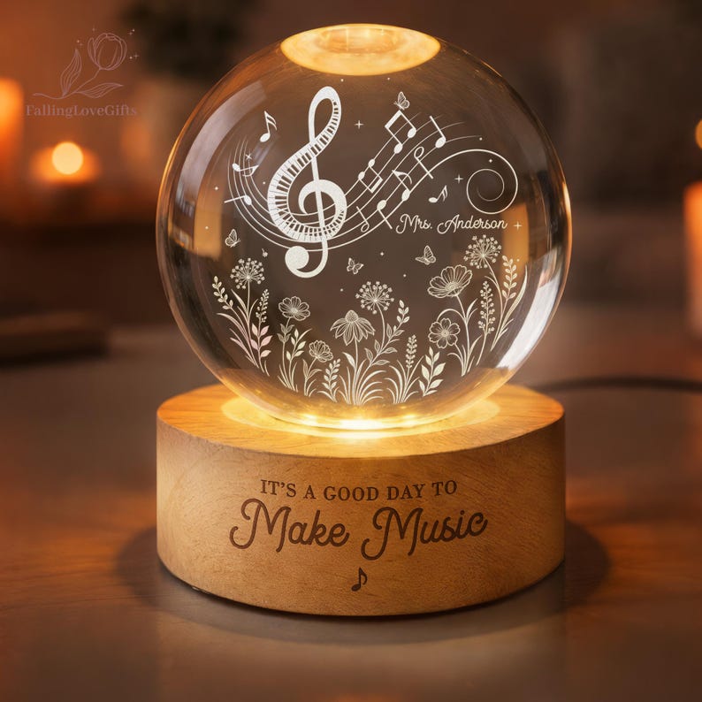Pu&ograve; includere: Una sfera di vetro illuminata con note musicali e motivi floreali, appoggiata su una base di legno. La base recita "IT'S A GOOD DAY TO Make Music". La sfera si illumina dall'interno, creando un'atmosfera calda e invitante.