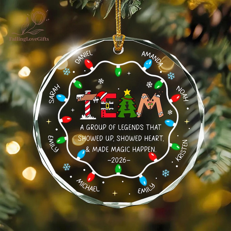 May include: A circular clear glass Christmas ornament featuring a string of colorful holiday lights around the perimeter. The center displays the word TEAM with festive graphics, the text A GROUP OF LEGENDS THAT SHOWED UP, SHOWED HEART, & MADE MAGIC HAPPEN. -2026-, and several names.