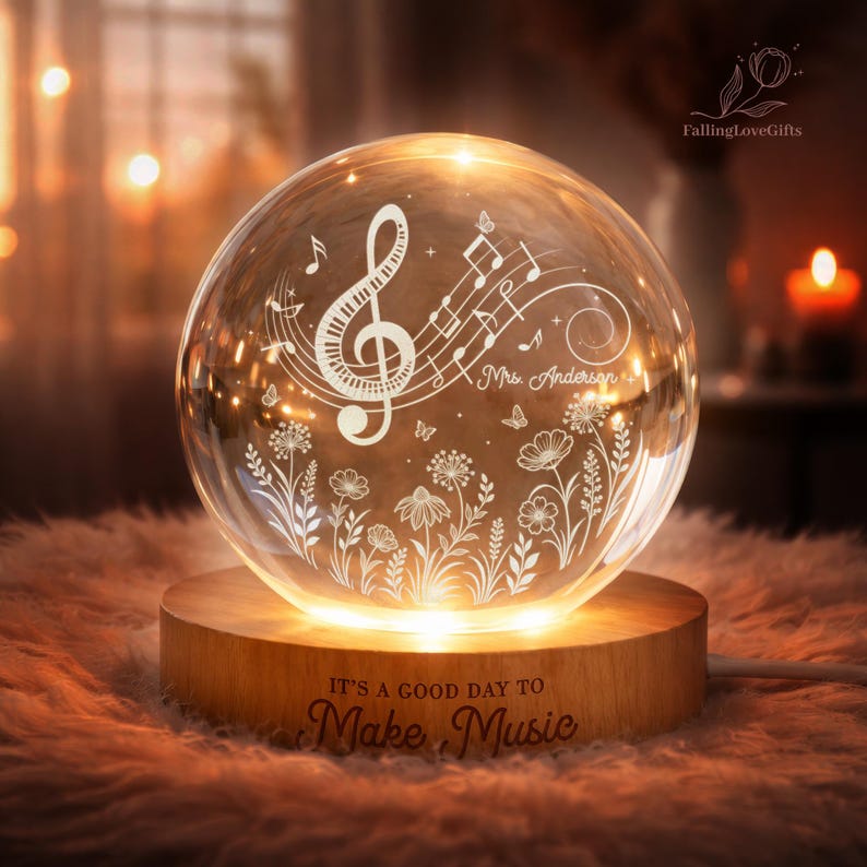 Pu&ograve; includere: Una sfera di vetro luminosa con motivi musicali e floreali, appoggiata su una base di legno. La sfera presenta una chiave di violino, note musicali, farfalle e fiori. La base riporta la scritta "IT'S A GOOD DAY TO Make Music".