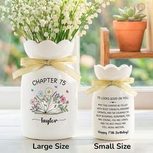 May include: Two white ceramic vases with scalloped tops and gold ribbon. The larger vase has "CHAPTER 75" and "Taylor" printed on it, with a floral and book design. The smaller vase says "75 LOOKS GOOD ON YOU" and a birthday message.