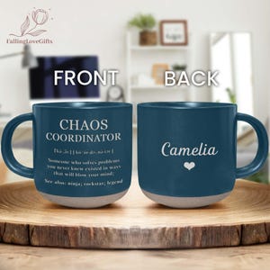 May include: A dark blue ceramic mug with a grey base. The front of the mug reads "CHAOS COORDINATOR" with a definition. The back of the mug has the name "Camelia" and a heart symbol.