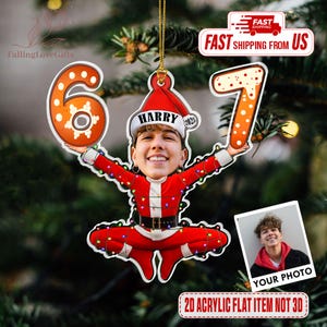 May include: A personalized Christmas ornament featuring a photo of a person dressed as Santa Claus, holding the numbers 6 and 7. The ornament is red and white, with the name "HARRY" on the hat. The text "2025" is also on the hat. The ornament is hanging on a Christmas tree.