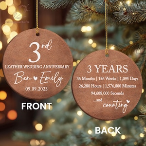 May include: Two round, brown, leather-textured ornaments with gold hanging strings. The front displays 3rd LEATHER WEDDING ANNIVERSARY, Ben and Emily, and 09.09.2023. The back lists 3 YEARS, 36 Months, 156 Weeks, 1,095 Days, 26,280 Hours, 1,576,800 Minutes, 94,608,000 Seconds, and ...and counting.
