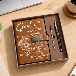 May include: A brown leather journal set in a gift box. The journal cover features the words "God says I am" and floral illustrations. The set includes a pen and a ballpoint pen. The journal also has the words "Saved, Peaceful, Hopeful, Image, Abundant".