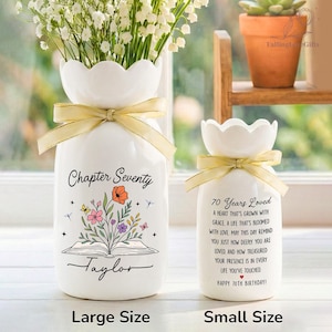 May include: Two white ceramic vases with scalloped rims and yellow ribbons. The larger vase features an open book illustration with flowers and the text "Chapter Seventy Taylor". The smaller vase displays the text "70 Years Loved" and a poem.