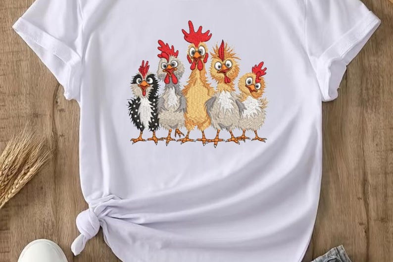 A white t-shirt with a colorful embroidered design of five cartoon chickens in various poses and colors.