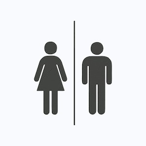 Op de afbeelding: Een zwart-wit toiletbord met een verticale lijn die een vrouwelijk en een mannelijk silhouet scheidt. De figuren zijn eenvoudig, wat wijst op aparte toiletten.