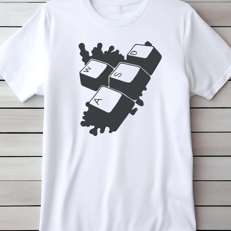 Peut inclure: T-shirt blanc avec un motif noir repr&eacute;sentant les touches de clavier W, A, S et D. Les touches sont regroup&eacute;es avec un fond sombre &eacute;clabouss&eacute;. Le t-shirt est fait d'une mati&egrave;re douce.