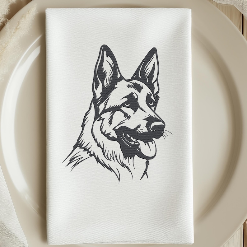 May include: White cloth napkin featuring a black and white illustration of a German Shepherd dog's head. The dog is depicted in profile, with its tongue slightly out. The napkin is folded and placed on a beige plate.