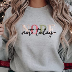 May include: A light gray sweatshirt with the embroidered text "NOPE not today". The word "NOPE" is in a pastel color scheme, with the letters in pink, green, and beige. The phrase "not today" is in a black script font.