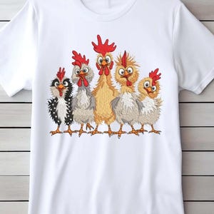 A white t-shirt with a graphic design of five cartoon chickens with red combs and wattles on their heads.