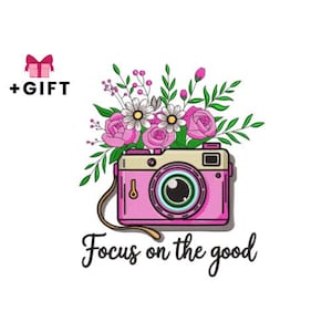May include: Pink camera illustration with a bouquet of flowers on top and the phrase "Focus on the good" below. The camera has a tan top and a brown strap. A pink gift box with a bow and the word "+GIFT" are in the upper left corner.