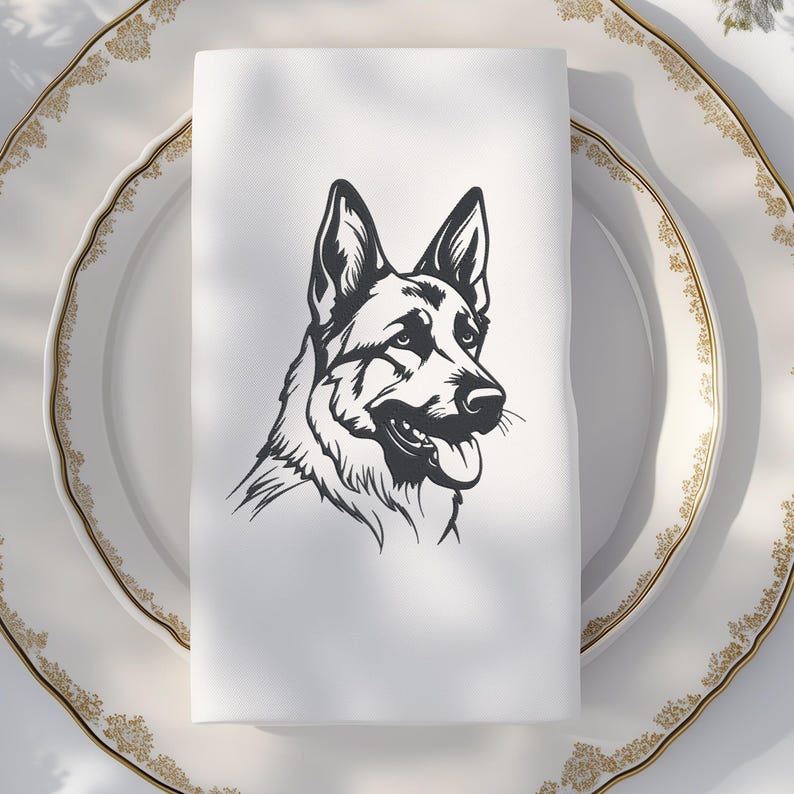 May include: A white cloth napkin featuring a black and white illustration of a German Shepherd dog's head. The napkin is folded and placed on a white plate with a gold rim. The dog's portrait shows its tongue and detailed fur.