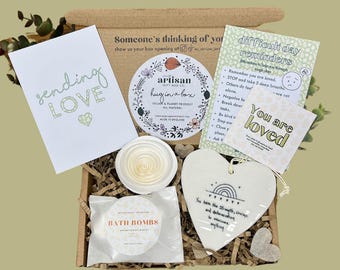 May include: A brown cardboard box filled with self-care items. The box contains a card that says "sending love", a white ceramic heart with the text "You are loved", a white ceramic dish with a spiral design, a white bath bomb, and a white card with the text "difficult day reminders".