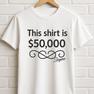 May include: White t-shirt with the text "This shirt is $50,000" in black, along with a decorative flourish and the name "Shisgama" in a script font. The shirt is hanging on a wooden hanger against a white brick wall.