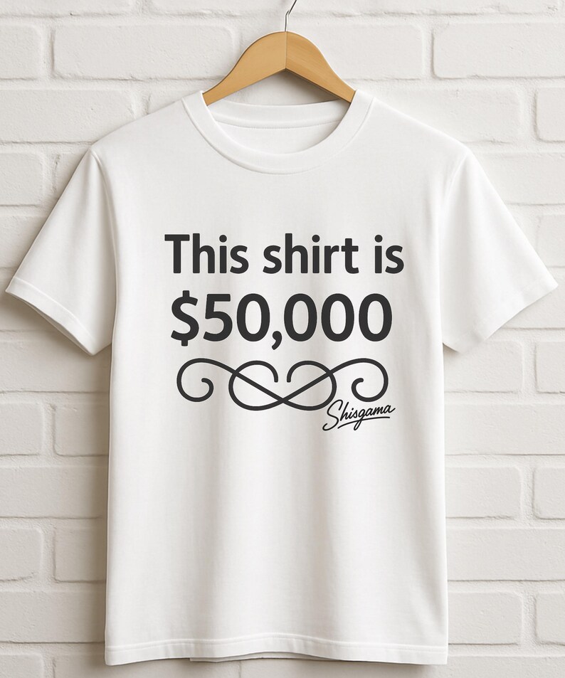 May include: White t-shirt with the text "This shirt is $50,000" in black, along with a decorative flourish and the name "Shisgama" in a script font. The shirt is hanging on a wooden hanger against a white brick wall.