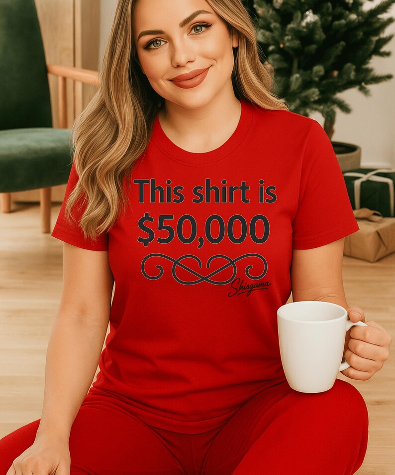 May include: Red t-shirt with the text "This shirt is $50,000" in black, along with a decorative swirl and the brand name "Shugama". The shirt is part of a red outfit and is paired with a white mug.
