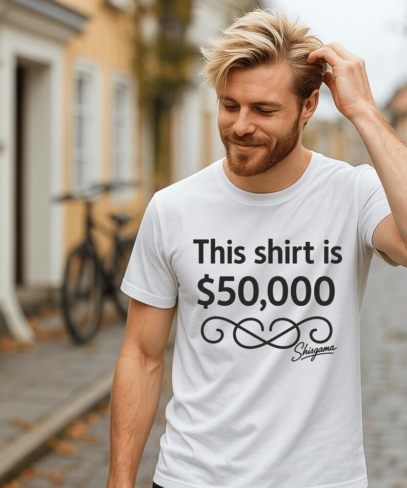 May include: White crew neck t-shirt with the text "This shirt is $50,000" in black. Below the text is a decorative swirl design and the brand name "Shisgama". The shirt is being worn.