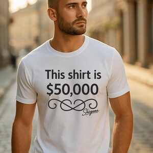 May include: White t-shirt with the text "This shirt is $50,000" in black. Below the text is a stylized infinity symbol and the brand name "Shisgama". The shirt is a crew neck style.