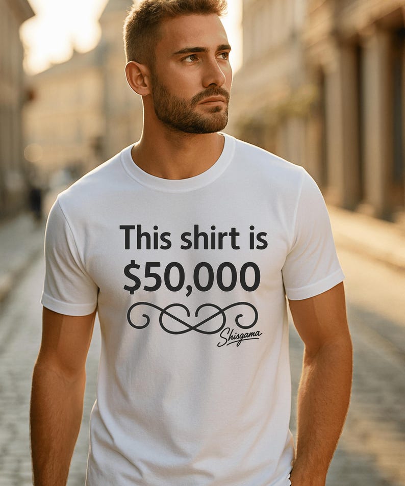 May include: White t-shirt with the text "This shirt is $50,000" in black. Below the text is a stylized infinity symbol and the brand name "Shisgama". The shirt is a crew neck style.