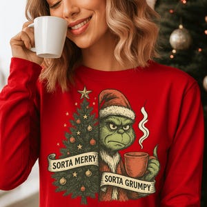Könnte beinhalten: Rotes Langarmshirt mit einem Weihnachtsbaum- und Grinch-Charakter-Design. Der Grinch hält eine Tasse, der Text lautet "Sorta Merry Sorta Grumpy". Ein festliches Urlaubs-Bekleidungsstück.