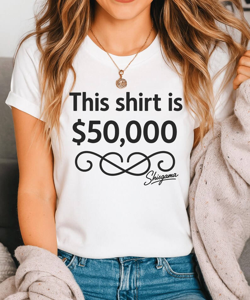 May include: White t-shirt with the text "This shirt is $50,000" in black, along with a decorative swirl and the word "Shisgama" in a script font. The shirt is short-sleeved.