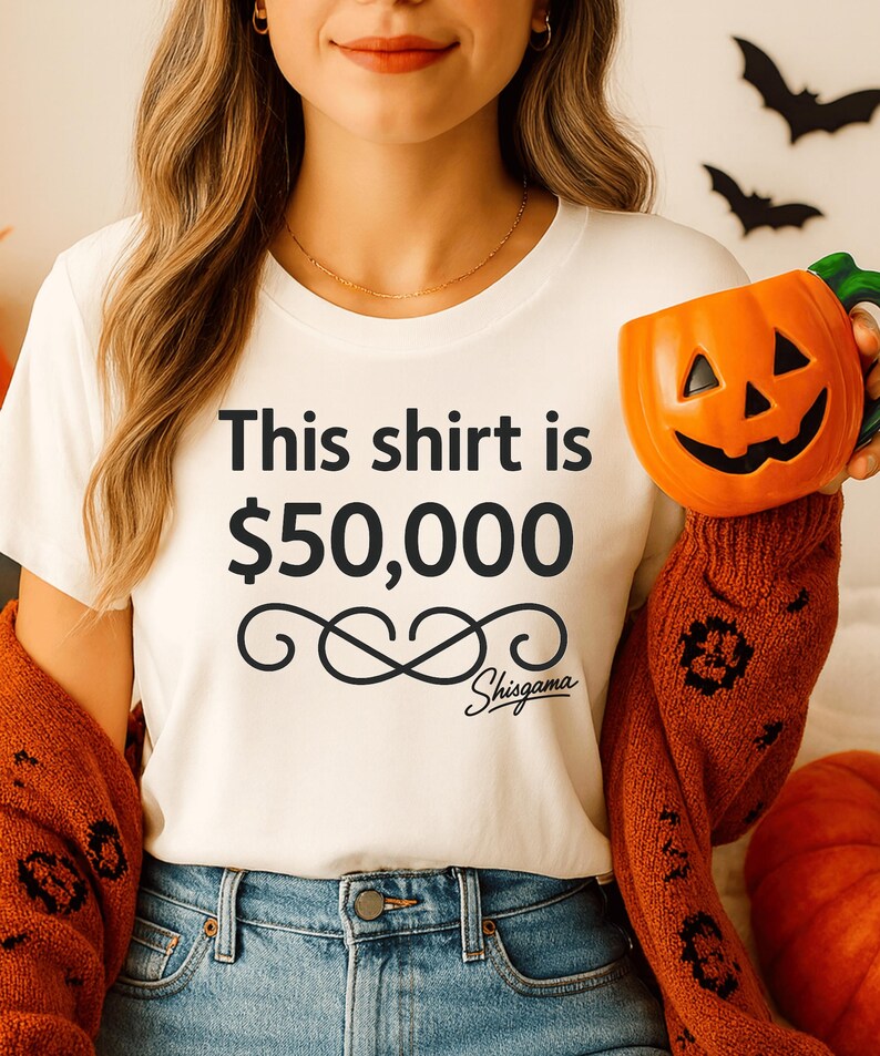 May include: White t-shirt with the text "This shirt is $50,000" and a decorative swirl design, with the brand name "Shisgama" below. The person is wearing blue jeans and an orange sweater. A ceramic pumpkin mug is held in the right hand.