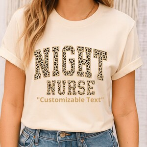 Può includere: T-shirt color crema con la scritta "NIGHT NURSE" in un design a stampa leopardata. Sotto, la frase "Customizable Text". La maglietta è abbinata a jeans blu.