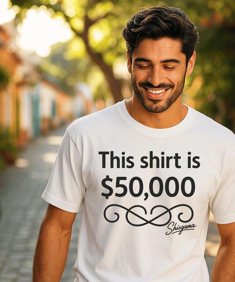 May include: White t-shirt with the text "This shirt is $50,000" in black. The shirt also features a decorative swirl design and the word "Shisgama" in script. The shirt is being worn by a person.