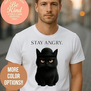 Può includere: T-shirt bianca con un gatto nero con bombetta e la scritta "STAY ANGRY". La maglietta presenta anche il testo "MORE COLOR OPTIONS!!" e "Be Kind" con "21 SELF-CARE QUOTES (PDF)" in un cerchio rosa.