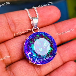 May include: A round, faceted pendant featuring a vibrant, iridescent gemstone with deep blue, purple, and green flashes. The stone is set in a silver-toned metal prong setting and hangs from a delicate silver-toned chain necklace.