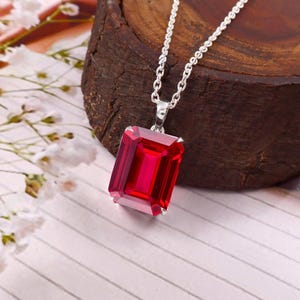 Pode incluir: Um colar de prata com um grande pendente retangular de pedra preciosa vermelho vibrante com lapidação esmeralda. O pendente é preso por uma argola de prata simples a uma corrente de prata fina, exibindo uma superfície facetada.