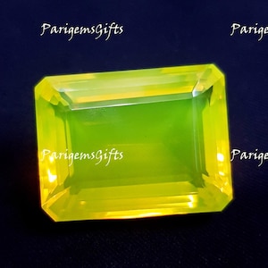 Pode incluir: Uma gema retangular e facetada com um tom vibrante amarelo-esverdeado. A gema está colocada sobre um fundo azul escuro, com o texto "ParigemsGifts" em escrita branca nos cantos. As bordas da gema são bem definidas, refletindo a luz.