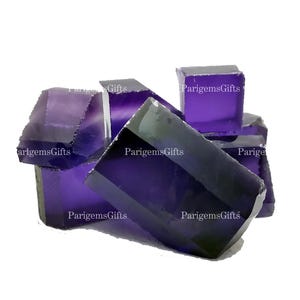 May include: A collection of deep purple amethyst crystals. The crystals have a faceted, geometric shape and a polished, reflective surface. The image includes the text "ParigemsGifts" in white.